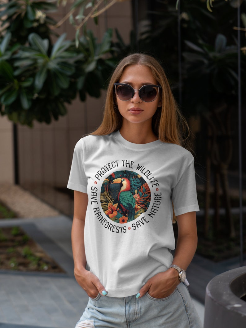 May include: White t-shirt with a colorful graphic of a toucan in a rainforest setting. The graphic is surrounded by the text "Protect the Wildlife Save Rainforests Save Nature".