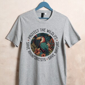 May include: Gray t-shirt with a circular graphic featuring a toucan in a rainforest setting. The text around the graphic reads "Protect the Wildlife, Save Rainforests, Save Nature."