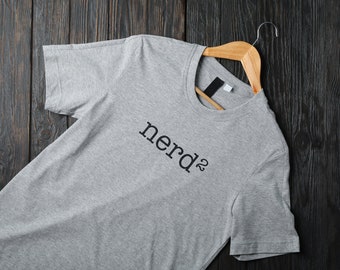 May include: A gray t-shirt with the word "nerd" printed on it. The shirt is hanging on a wooden hanger.