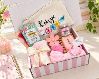 May include: A gift box containing a beige canvas pouch with the name Kenzie and floral graphics, a face mask, a pink sugar scrub, a flower-shaped hair clip, a pink bath bomb, a pink soap bar, a pink headband, and a beaded bracelet.