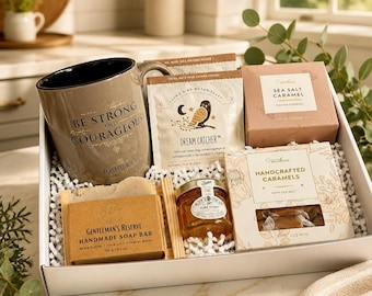 May include: A gift box containing a beige mug with the text BE STRONG AND COURAGEOUS JOSHUA 1:9, a packet of Dream Catcher herbal tea, a box of Sea Salt Caramel cookies, a bar of Gentleman's Reserve handmade soap, a jar of honey, and caramels.