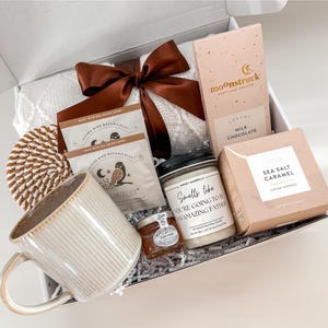 May include: A gift box filled with a variety of items, including a mug, chocolate bar, candle, cookies, tea, and honey. The box is tied with a brown ribbon. The candle reads "Smells like you're going to be an amazing father."