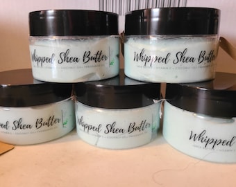 May include: A stack of six small jars of whipped shea butter with black lids. The jars are filled with a light blue cream and labeled "Whipped Shea Butter". The ingredients include shea butter, vitamin E, coconut oil, and fragrance oil.