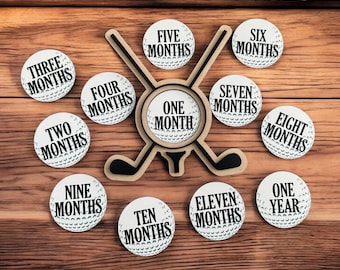 May include: White golf ball-shaped ornaments with black text indicating the number of months. The ornaments are arranged around a wooden golf club cutout. The text includes "One Month", "Two Months", "Three Months", "Four Months", "Five Months", "Six Months", "Seven Months", "Eight Months", "Nine Months", "Ten Months", "Eleven Months", and "One Year".
