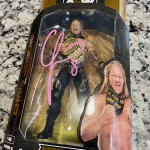 May include: A black and gold action figure of a wrestler holding a championship belt. The figure is in a plastic display case with a gold background. The figure is labeled "Chris Jericho" and "Unrivaled Collection".