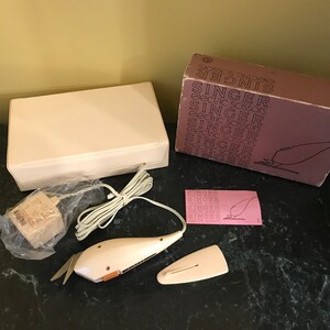 May include: A white Singer electric scissors set with a white storage case, a power cord, a power adapter, and a pink instruction sheet. The box is labeled "Singer Electric Scissors".