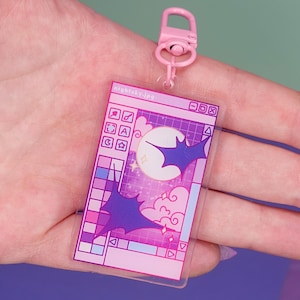 Könnte beinhalten: Ein pinkfarbener und violetter Acryl-Anhänger mit einem Computer-Interface-Design, einem Mond, Fledermäusen und Wolken. Er ist an einem pinkfarbenen Verschluss befestigt. Der Text "nightsky.jpg" ist auf dem Anhänger sichtbar.