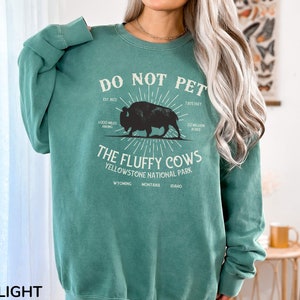 May include: Light green sweatshirt with a graphic print of a bison and the text "Do Not Pet The Fluffy Cows Yellowstone National Park Est 1872 1000 Miles Hiking 7,875 Feet 22 Million Acres Wyoming Montana Idaho"