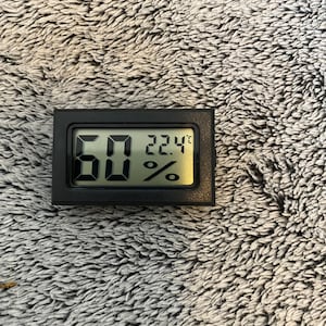 May include: A black digital hygrometer with a white display showing a temperature of 22.4 degrees Celsius and a humidity level of 60%.
