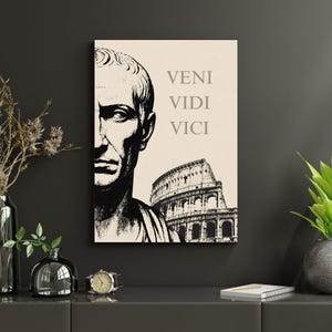 May include: A rectangular wall art print on a light beige background featuring a black and white illustration of a Roman bust on the left and the Colosseum on the bottom right. The text VENI VIDI VICI is printed in black in the upper right area.