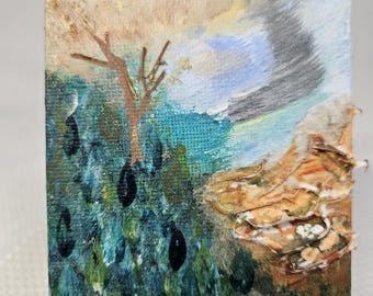 May include: A small abstract painting on canvas with a brown tree, blue and green water, and a gold and white textured area. The painting is on a small wooden easel.
