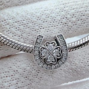 May include: A silver charm bracelet with a horseshoe charm featuring a four-leaf clover with clear cubic zirconia stones.