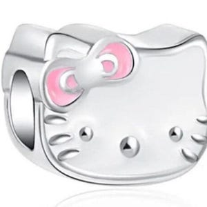 May include: A silver charm in the shape of Hello Kitty with pink ears and a pink bow.