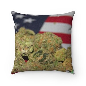 May include: A square pillow with a green and brown marijuana bud design on a red, white, and blue American flag background.