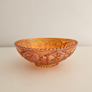 May include: A vintage amber glass bowl with a decorative, geometric pattern. The bowl has a scalloped edge and a slightly flared rim.