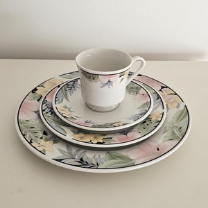 May include: A set of three white ceramic plates with a floral design in shades of pink, yellow, and green. The plates are nested together, with a matching white ceramic teacup and saucer in the center.