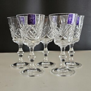 May include: Set of six clear crystal wine glasses with diamond and fan cut patterns. Each glass has a stem and a round base. The glasses have a purple and white label that reads "Edinburgh Crystal".