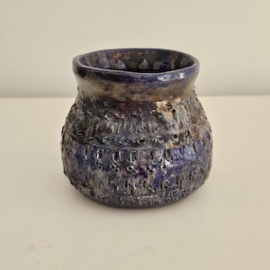 May include: A small, round, blue and brown ceramic vase with a textured surface.