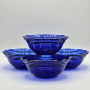May include: A set of three deep cobalt blue glass bowls arranged in a triangular formation. Each bowl features a series of horizontal concentric rings molded into the exterior surface, creating a ribbed texture around the circular rim and base.