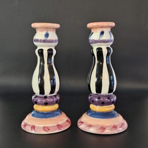 May include: A pair of ceramic candle holders with a black and white striped design. The holders have a pink, yellow, purple, and blue base.