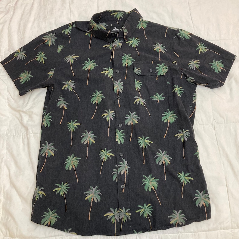 May include: Black short-sleeve button-down shirt with a palm tree pattern. The shirt features a chest pocket and a classic collar. The palm trees are green and tan, and the shirt is made of a soft material.