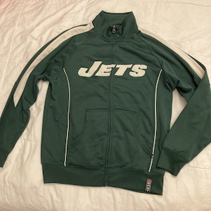 Op de afbeelding: Een groene jas met ritssluiting, witte accenten en het woord "JETS" op de borst. De jas heeft een hoge kraag, een voorzak en witte strepen op de mouwen. De jas is gemaakt van een glad, sportief materiaal.