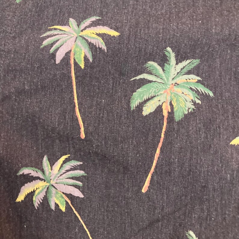 May include: Dark blue fabric with a repeating pattern of palm trees. The palm trees have green, yellow, and purple fronds and brown trunks. The overall design has a tropical theme.