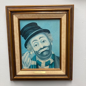 May include: Framed vintage painting of a sad clown with a blue and white striped scarf, black top hat, and a cigar. The painting has a gold frame and a light blue background. The clown's face is painted with traditional clown makeup.