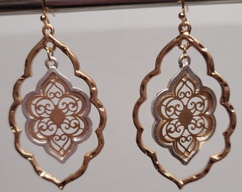 May include: A pair of gold and silver earrings with a filigree design. The earrings are shaped like a teardrop and have a delicate, intricate pattern.