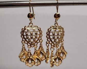 May include: A pair of gold heart-shaped dangle earrings with intricate filigree designs. The earrings have multiple delicate drops hanging from the heart.