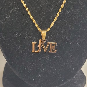 Op de afbeelding: Een gouden ketting met een hanger die "LOVE" spelt in een gestileerd lettertype.