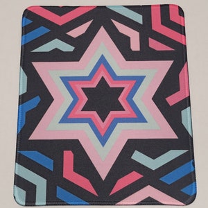 May include: A black mouse pad with a pink, blue, and white geometric star design. The star is surrounded by a black background with pink, blue, and white geometric shapes.