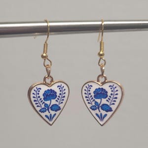 May include: A pair of gold heart-shaped earrings with a blue and white floral design.