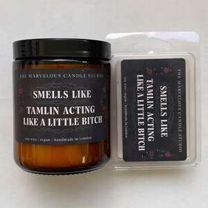 Puede incluir: Un juego de velas y cera fundida de The Marvelous Candle Studio. La vela est&aacute; en un frasco de vidrio marr&oacute;n con tapa negra. La etiqueta dice "Smells Like Tamlin Acting Like a Little Bitch." La cera fundida tiene el mismo texto.