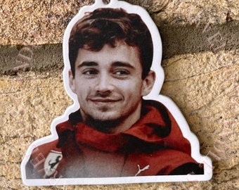May include: White car air freshener with a photo of a man wearing a red racing suit. The man is smiling and has short brown hair.