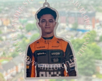 May include: A car air freshener featuring a photo of a race car driver wearing a black and orange racing suit with the words "android", "splunk", "ARROW", and "Cisco" on it.