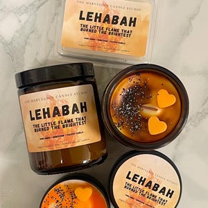 May include: An assortment of candles from The Marvelous Candle Studio. The candles are in various containers, including a wax melt, a jar, and tins. The candles have a warm, amber color and are decorated with heart-shaped wax accents and glitter. The text "LEHABAH" is visible.