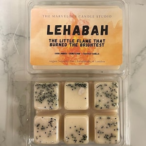 May include: A clear plastic container holding six wax melts. The melts are square, off-white, and speckled with black and silver glitter. The label reads "LEHABAH" and "THE LITTLE FLAME THAT BURNED THE BRIGHTEST."
