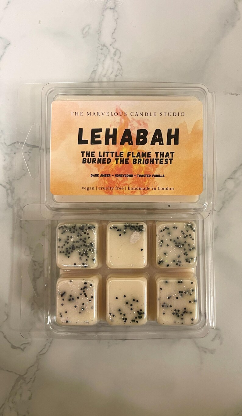 May include: A clear plastic container holding six wax melts. The melts are square, off-white, and speckled with black and silver glitter. The label reads "LEHABAH" and "THE LITTLE FLAME THAT BURNED THE BRIGHTEST."