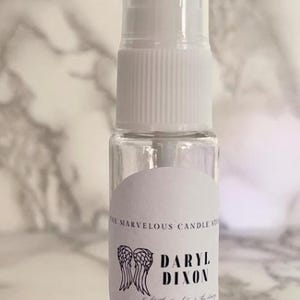 May include: A clear plastic bottle with a white spray nozzle and a white label. The label has a black and white illustration of angel wings and the text "Daryl Dixon Get the good out of the story".
