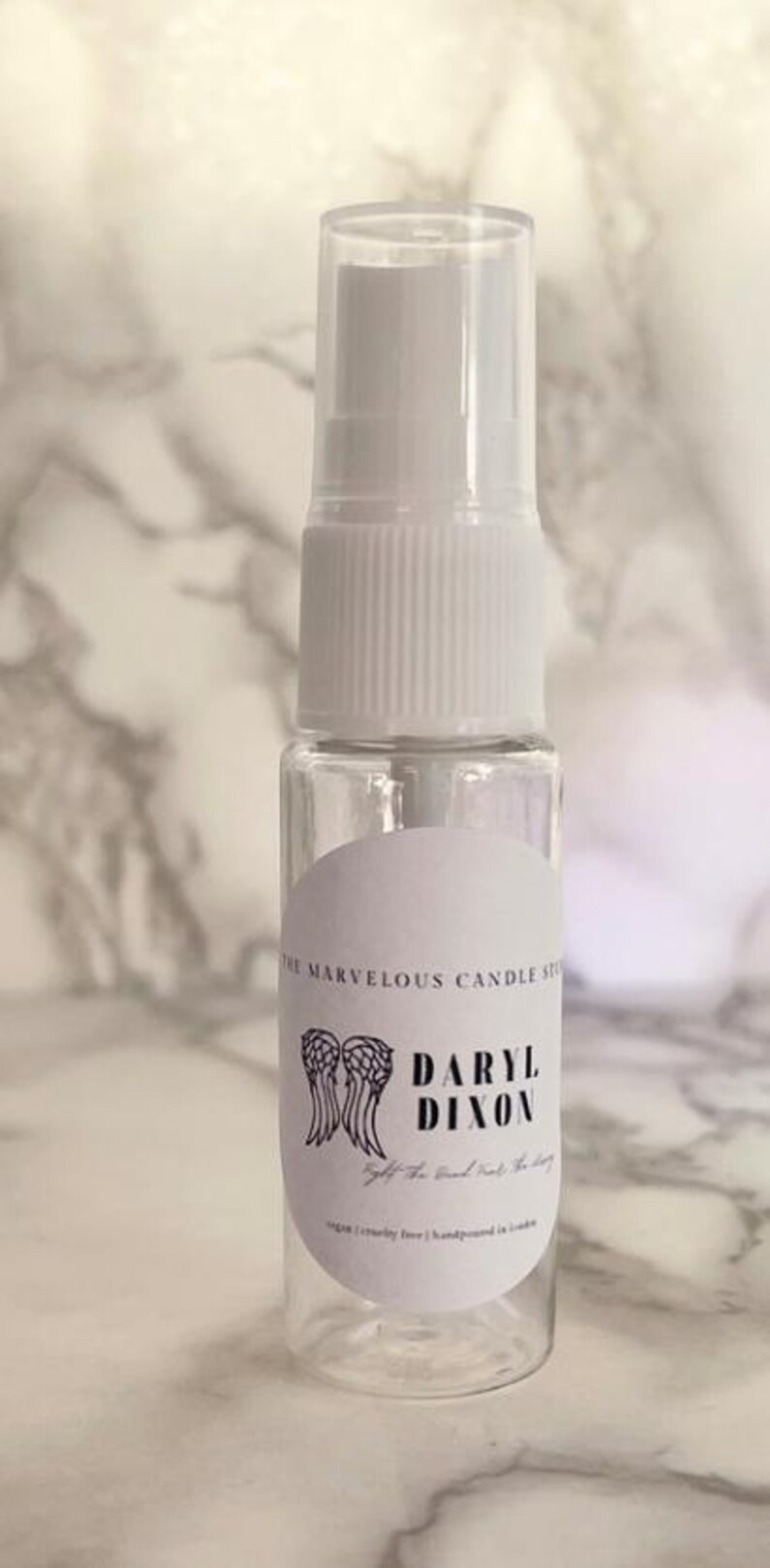 May include: A clear plastic bottle with a white spray nozzle and a white label. The label has a black and white illustration of angel wings and the text "Daryl Dixon Get the good out of the story".