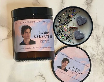 May include: Two soy wax candles with a black and white image of a man on the front. The text on the candle reads "The Marvelous Candle Studio Damon Salvatore Amberwoods Cedar - Musk Soy wax | Vegan | Cruelty free | Handpoured in London".