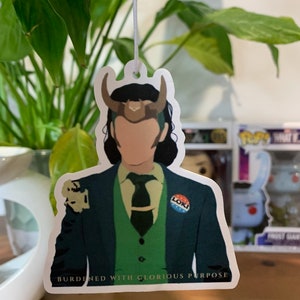 May include: A green, blue, and white button with the word "Loki" on it. The button is attached to a green suit jacket with a green vest and a green tie. The text "Burdened with Glorious Purpose" is printed below the image.