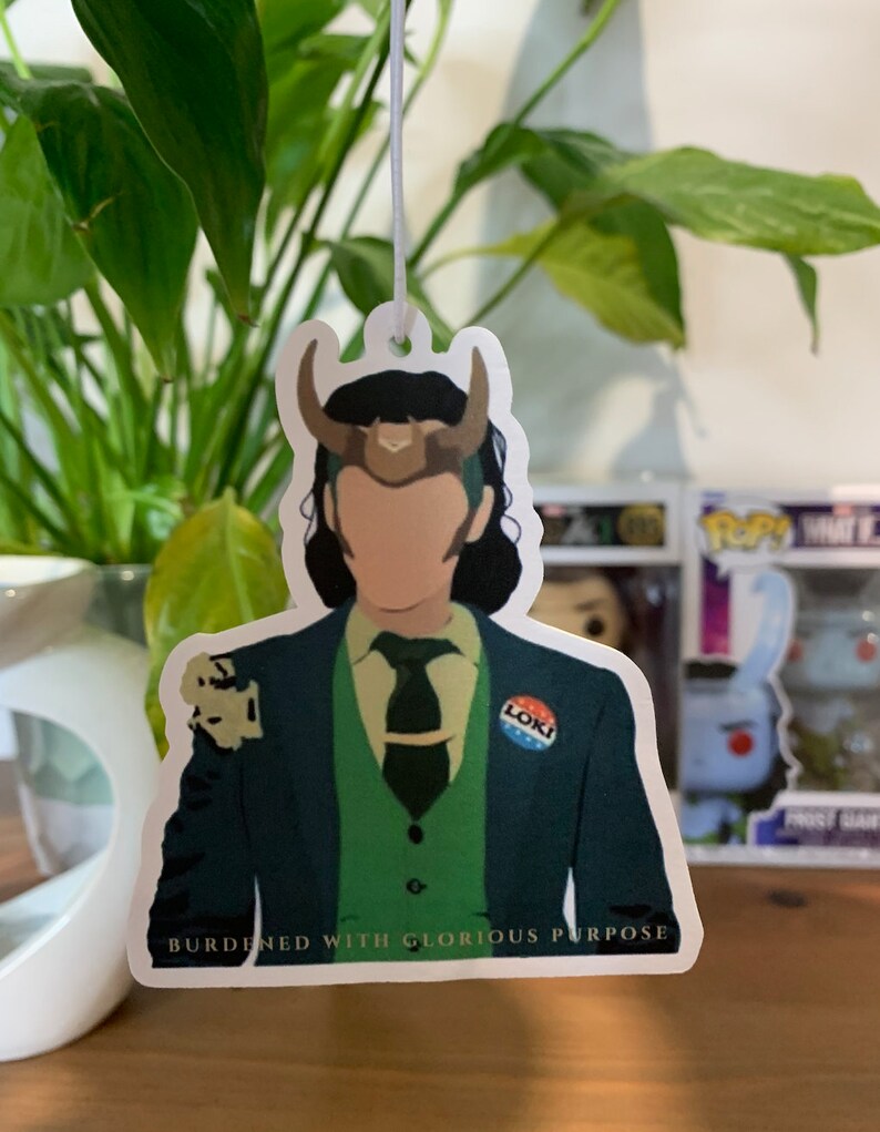 May include: A green, blue, and white button with the word "Loki" on it. The button is attached to a green suit jacket with a green vest and a green tie. The text "Burdened with Glorious Purpose" is printed below the image.