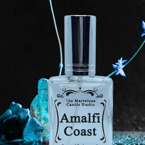 Puede incluir: Una botella de vidrio transparente con un pulverizador plateado y una etiqueta negra que dice "The Marvelous Candle Studio Amalfi Coast 15ml".