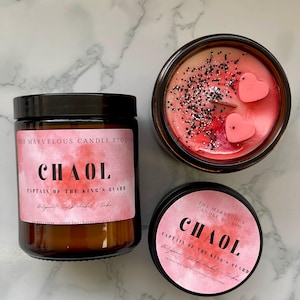 Puede incluir: Tres velas perfumadas con etiquetas rosas. La más grande está en un tarro marrón, la segunda en un tarro transparente y la más pequeña en una lata negra. Las etiquetas dicen "CHAOL" y "CAPTAIN OF THE KING'S GUARD".