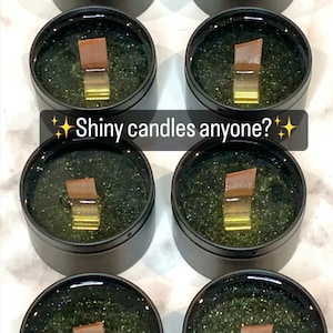 Puede incluir: Seis tarros de velas negros con purpurina verde y una mecha de madera marr&oacute;n. Los tarros est&aacute;n dispuestos en dos filas de tres. El texto "Shiny candles anyone?" est&aacute; superpuesto a la imagen.