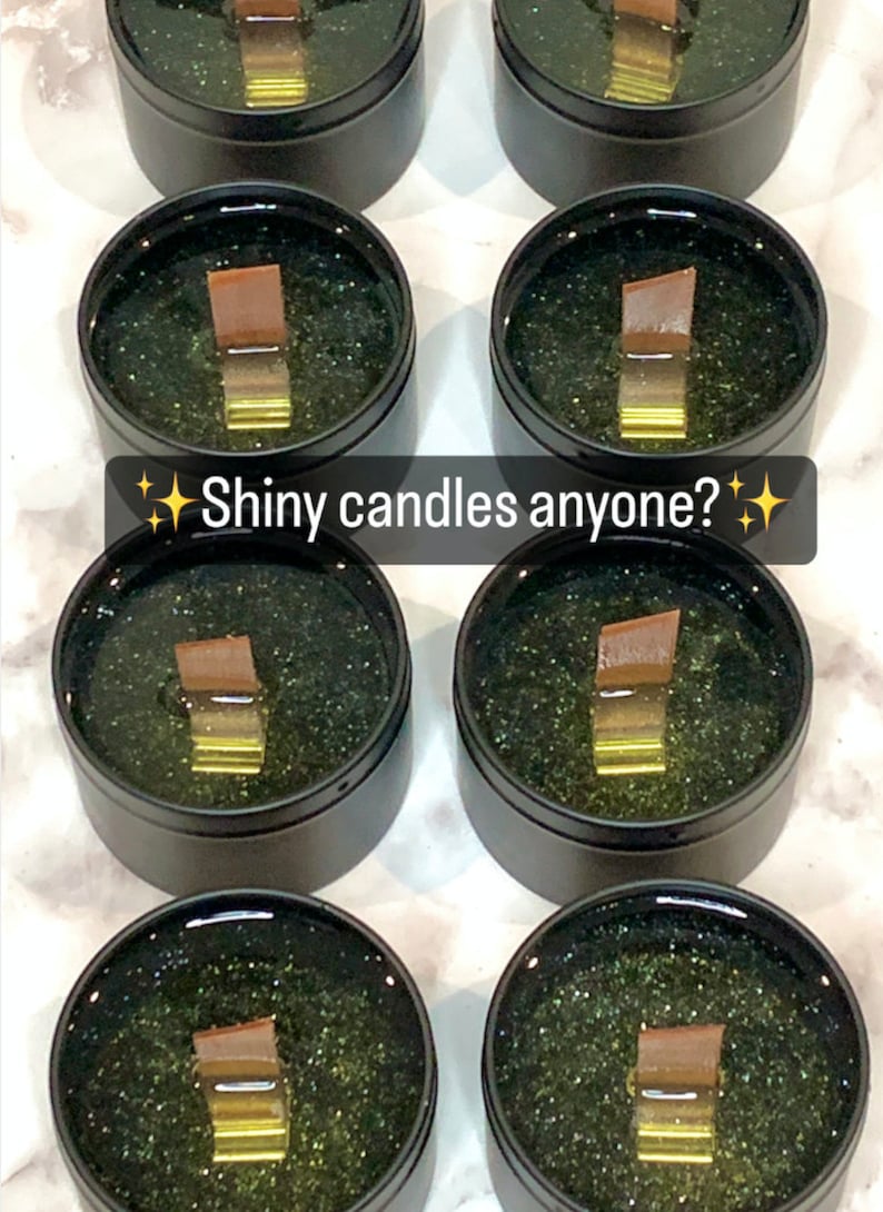 Puede incluir: Seis tarros de velas negros con purpurina verde y una mecha de madera marr&oacute;n. Los tarros est&aacute;n dispuestos en dos filas de tres. El texto "Shiny candles anyone?" est&aacute; superpuesto a la imagen.