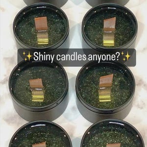 May include: Several small, round, black containers filled with a dark green substance and a wooden wick. The text "Shiny candles anyone?" is displayed in a white font with star accents.