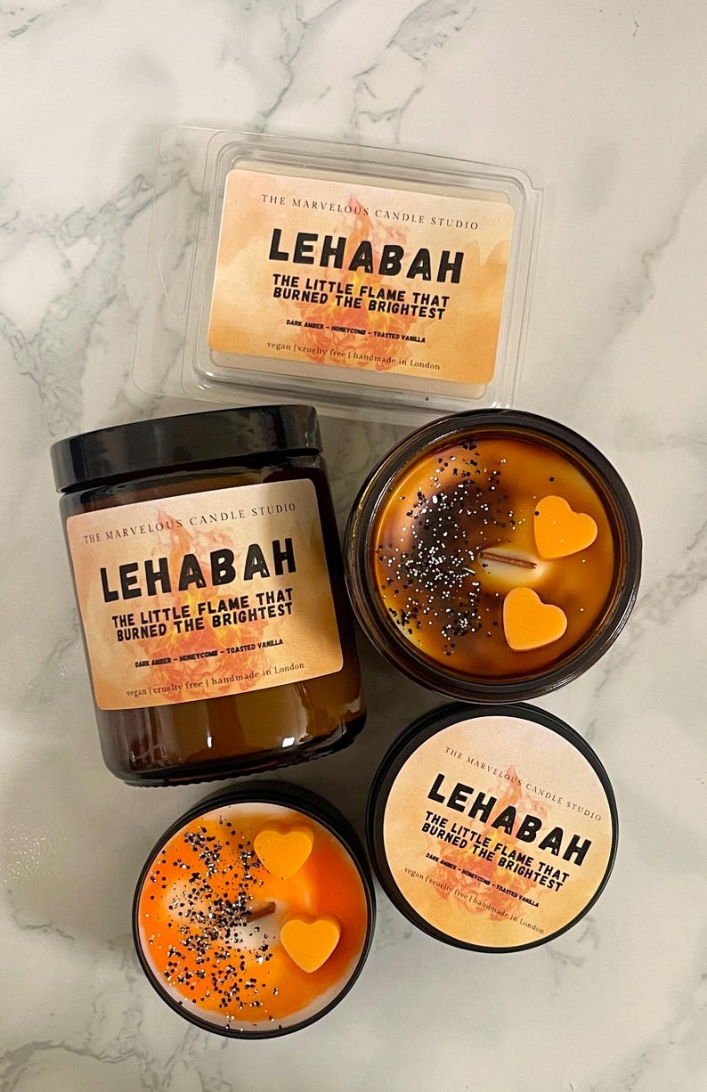 May include: An assortment of candles from The Marvelous Candle Studio. The candles are in various containers, including a wax melt, a jar, and tins. The candles have a warm, amber color and are decorated with heart-shaped wax accents and glitter. The text "LEHABAH" is visible.